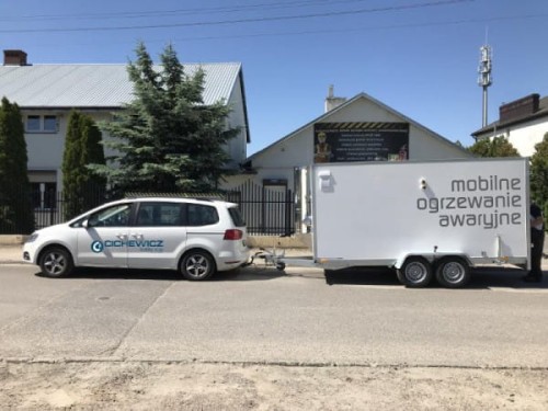 Mobilny system grzewczy na pellet - wynajem. Biały samochód osobowy i przyczepa z piecem.